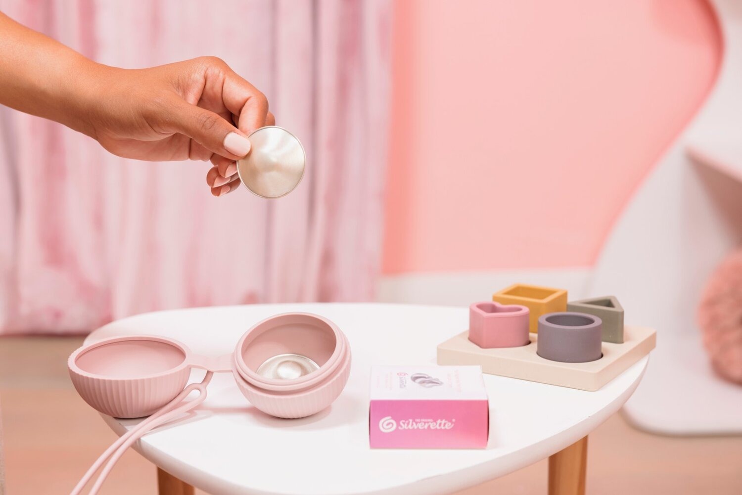 Mano che tiene una coppetta Silverette accanto alla custodia in silicone e alla confezione