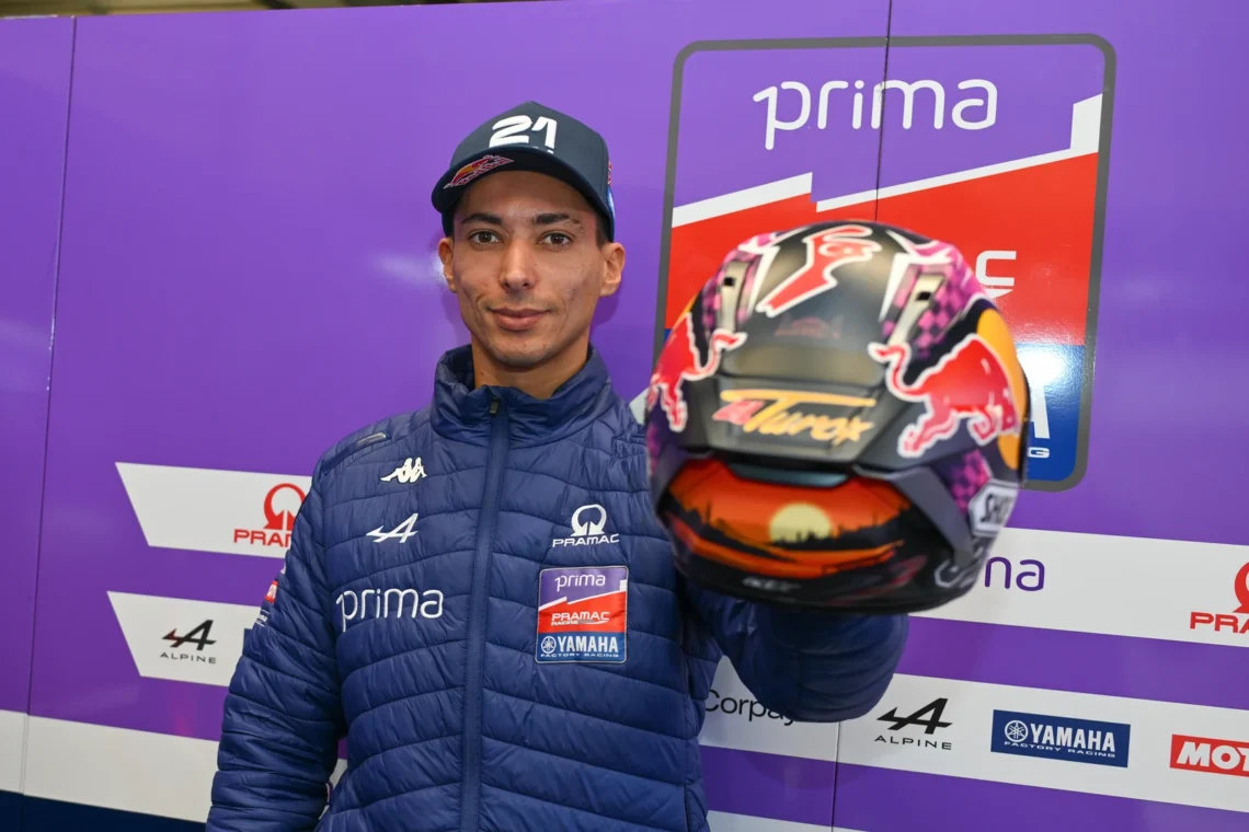 Toprak Razgatlioğlu sorridente con giacca Prima Pramac Yamaha Factory Racing mentre tiene in mano il casco speciale creato dalla community di MotoGP 26