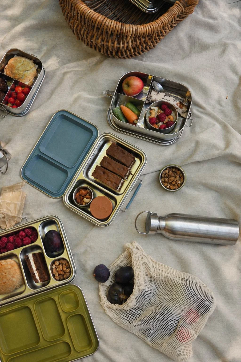 Composizione lifestyle sul prato con HAPS BOX, Steel Trio e snack freschi durante un picnic in famiglia