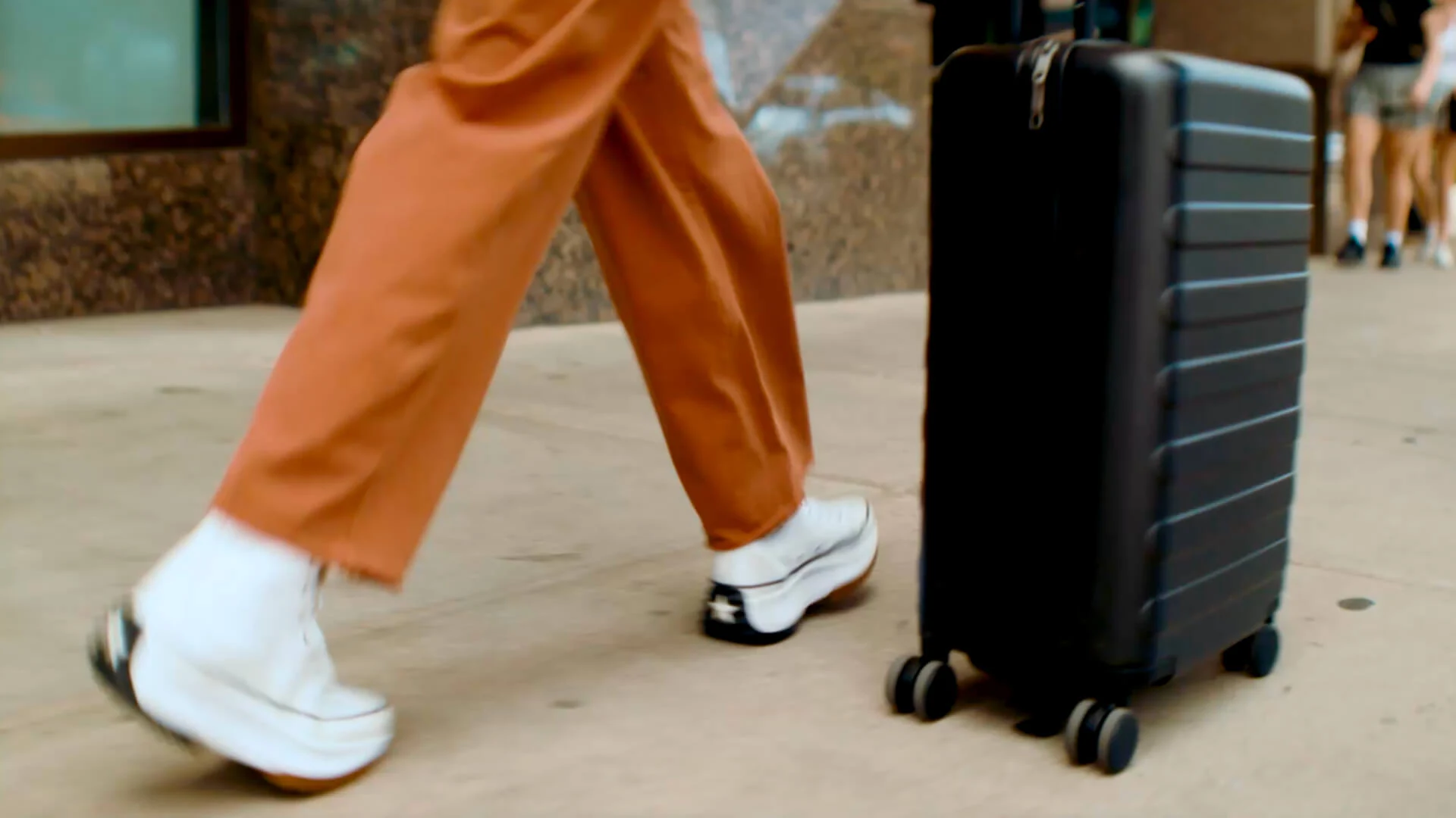Dettaglio di un viaggiatore contemporaneo che cammina in città con sneakers alla moda e trolley rigido da viaggio