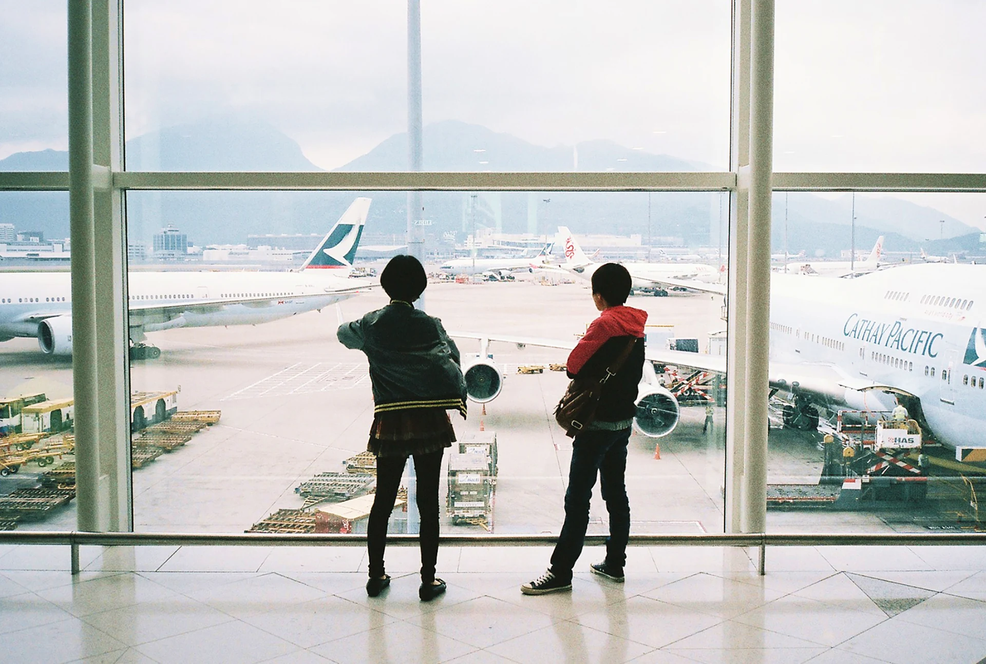Due giovani viaggiatori della Gen Z osservano gli aeroplani sulla pista dell'aeroporto dalla vetrata del terminal